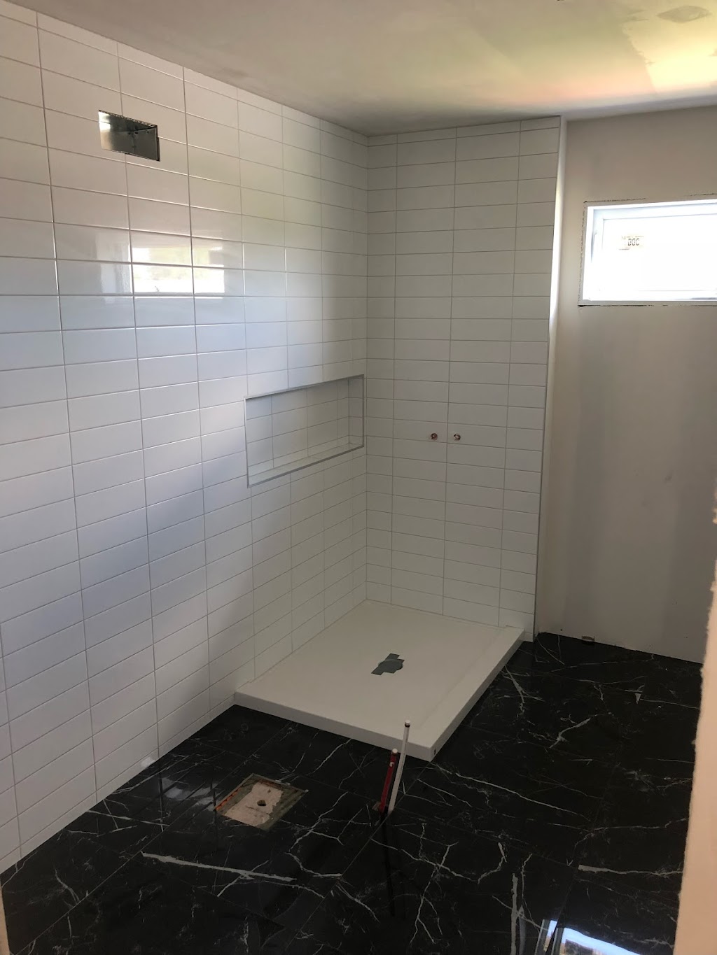 Douche en tuiles blanches avec niche encastrée et plancher effet marbre noir veiné blanc