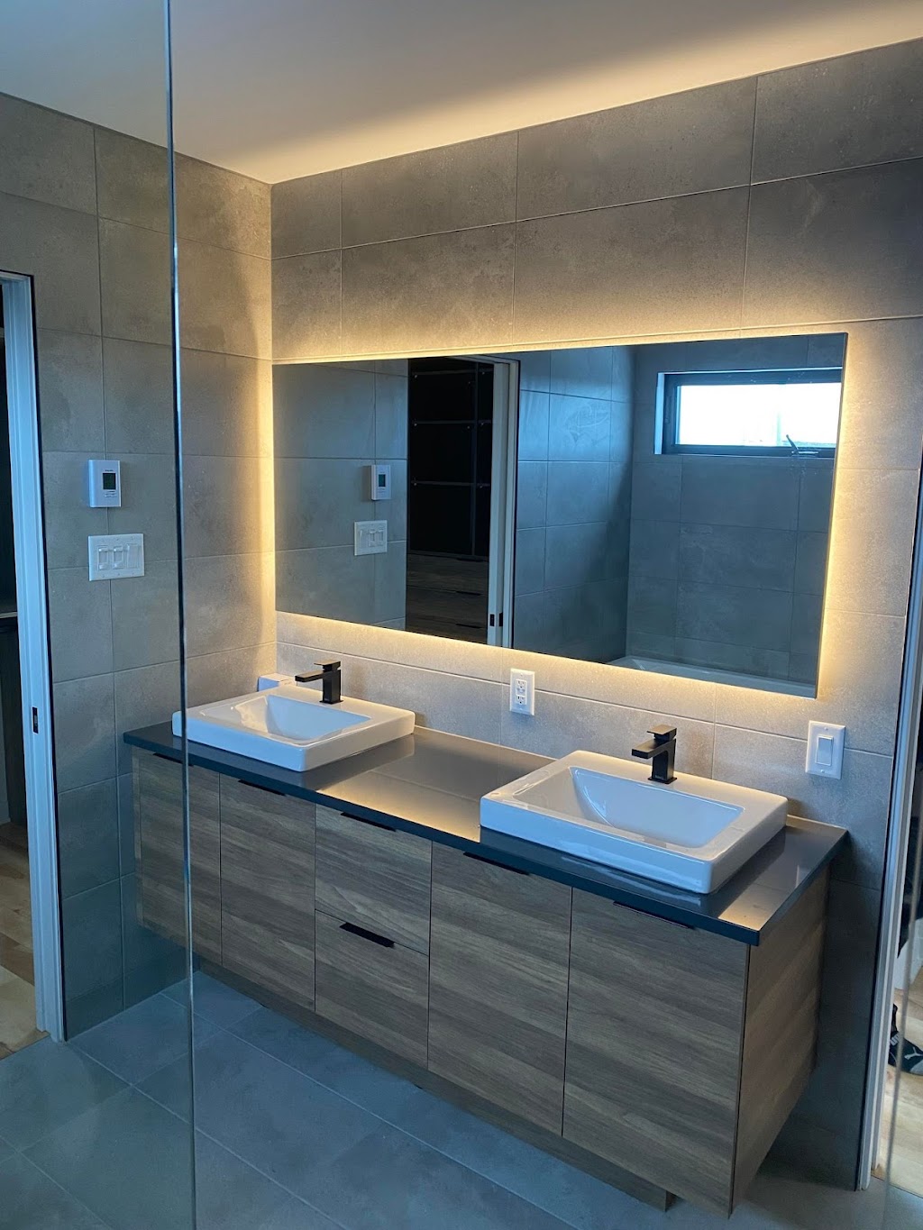 Mur et plancher en céramique grand format gris avec vanité double flottante et miroir DEL par Céramique Plus